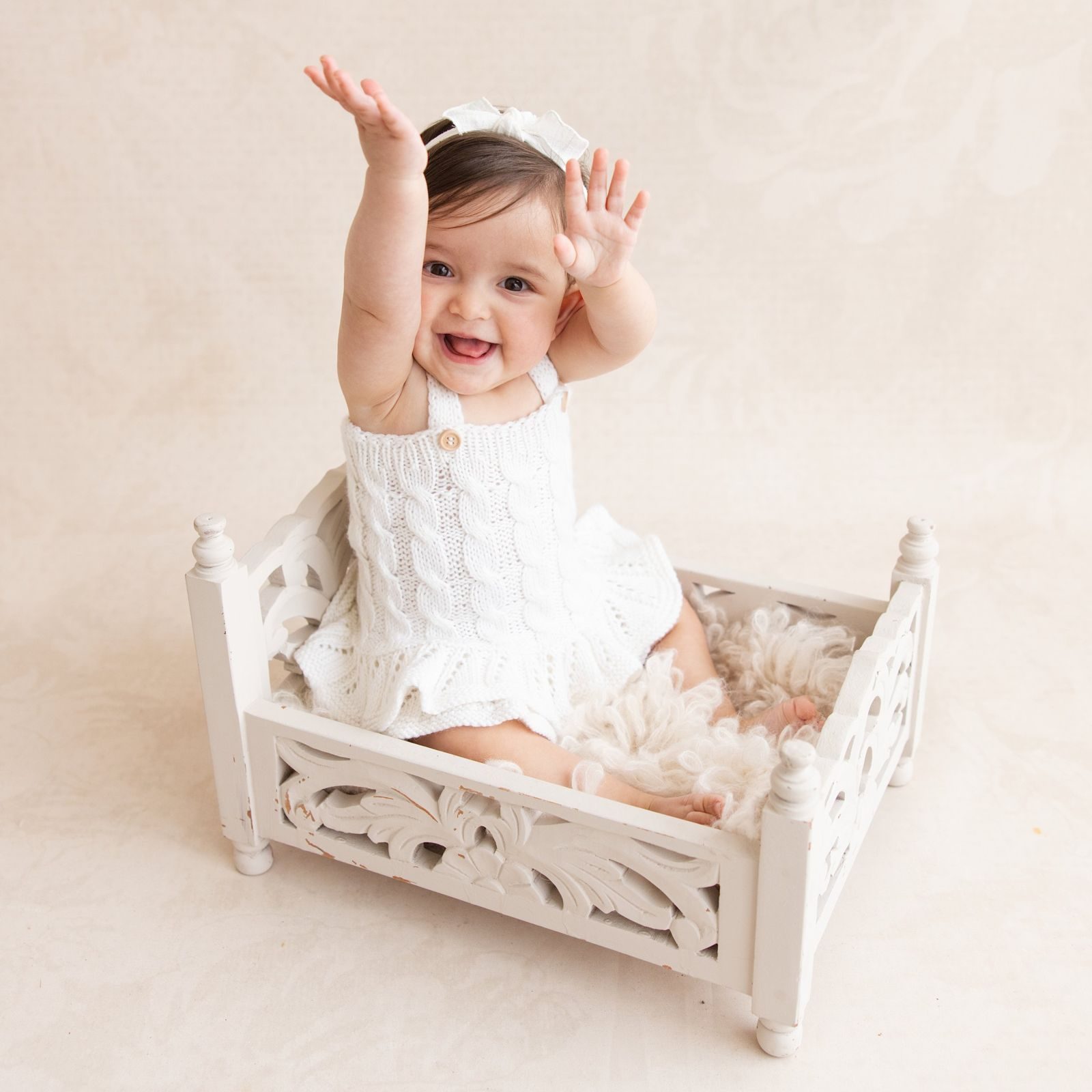 Laughing baby with her arms up in a small white bed