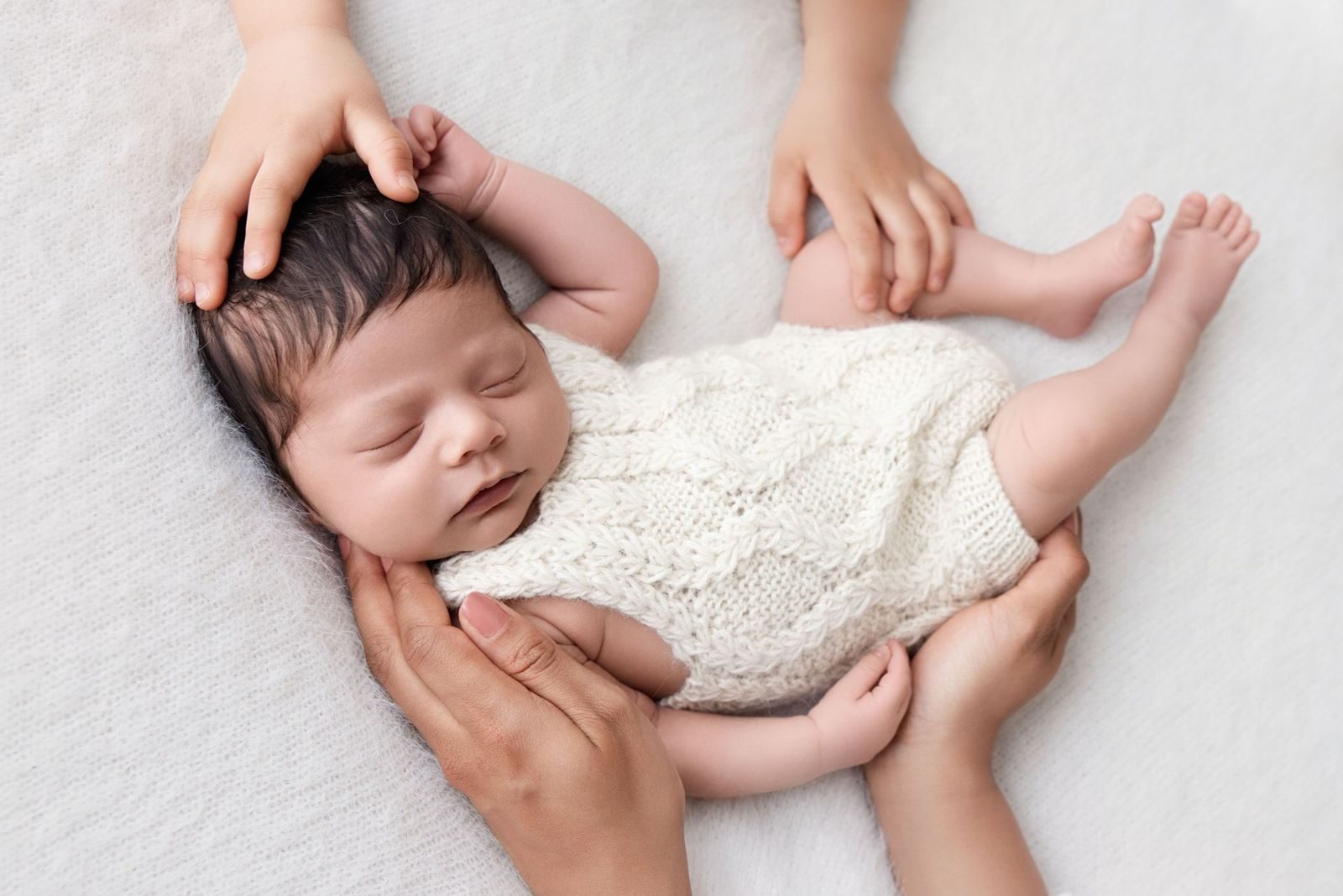 Newborn held by the hands of mother and big sister